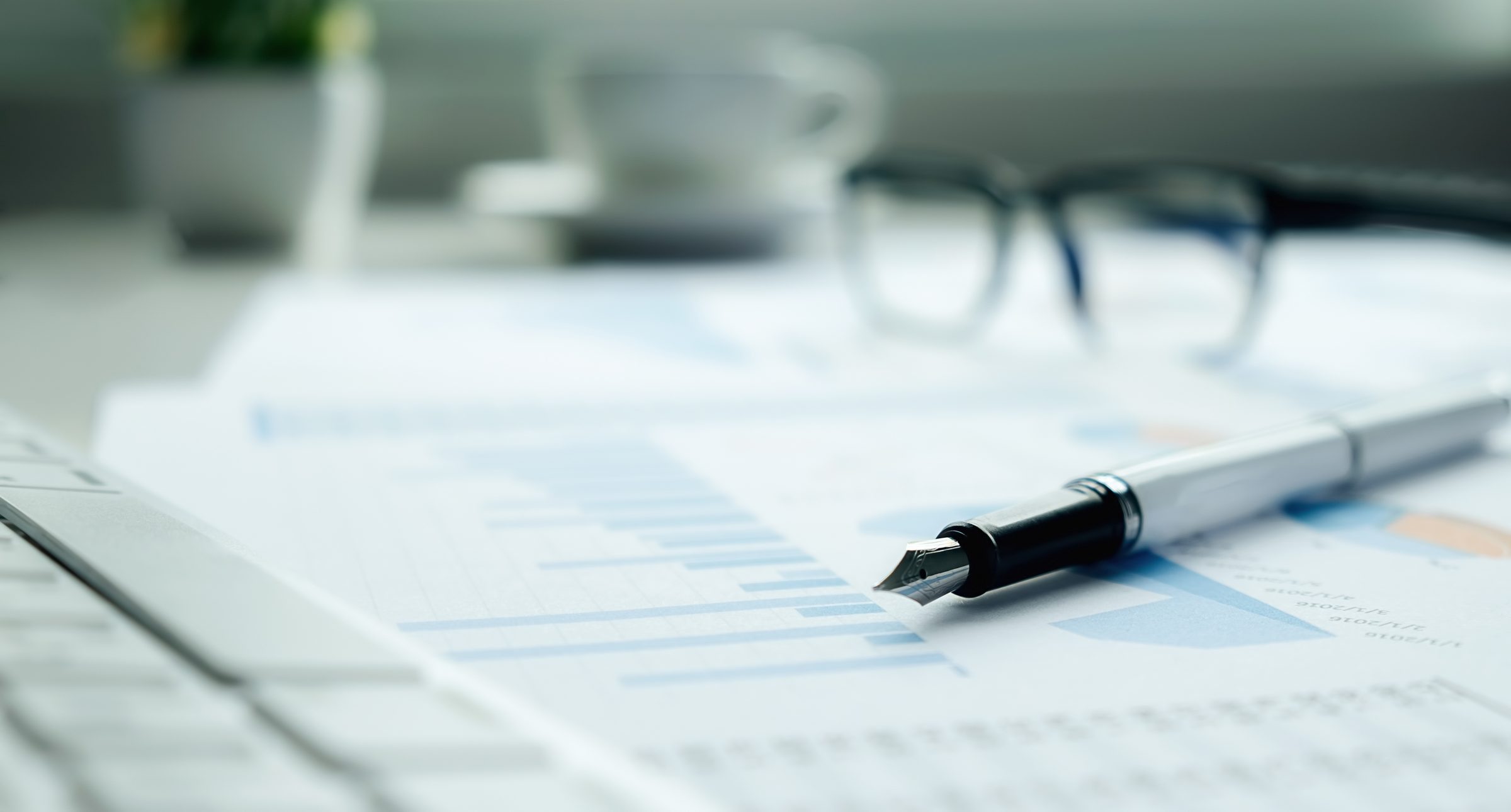 A report of charts on a desk with a pen and reading glasses